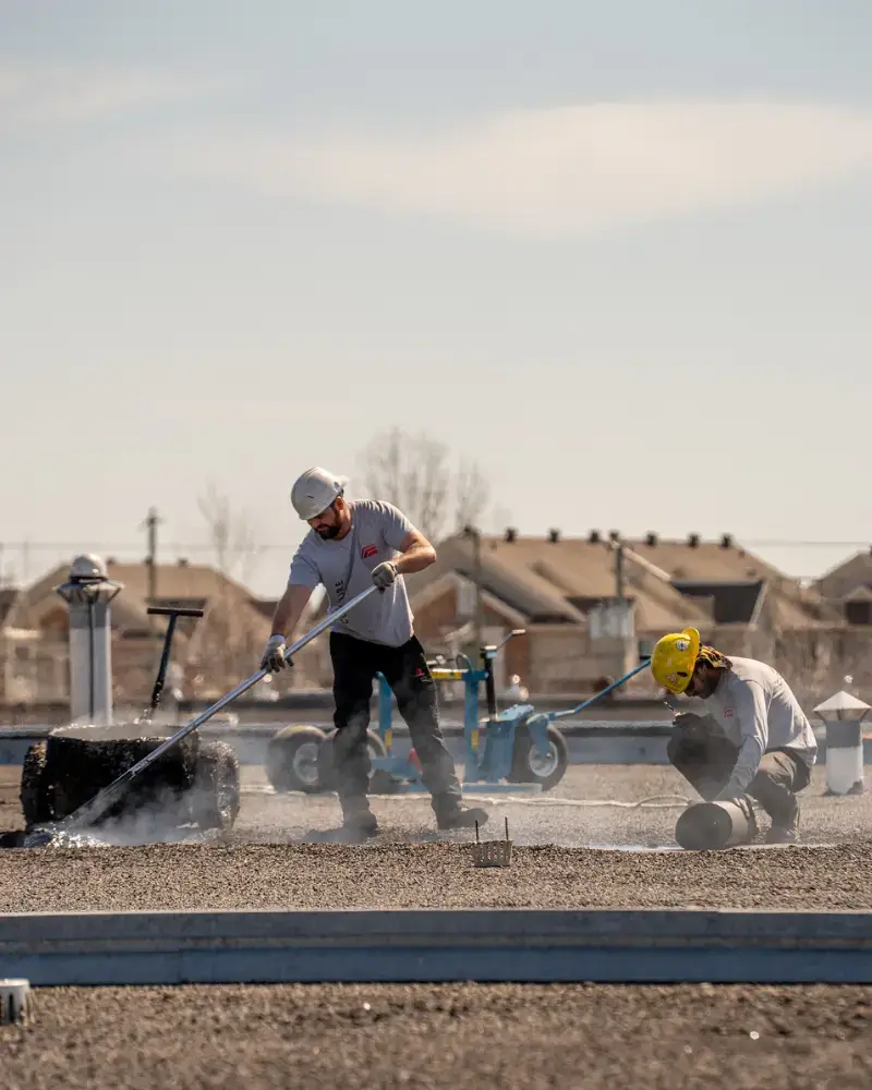 Techniciens effectuant une réparation de toiture plate avec membrane élastomère sur un bâtiment.